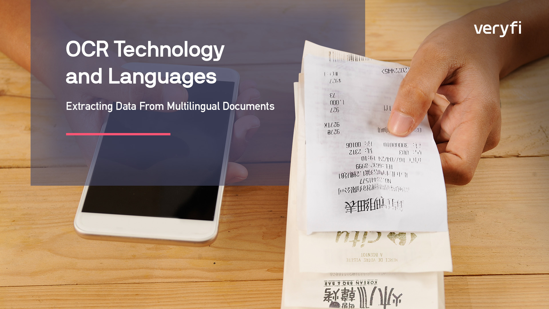 A hand holding receipts in different languages next to a mobile phone.